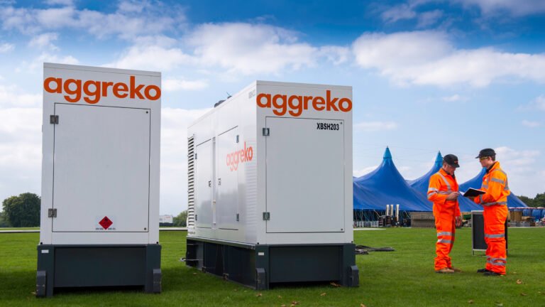 Aggreko mobile power generators installed on-site while two engineers in high-visibility safety gear review equipment and operations outdoors
